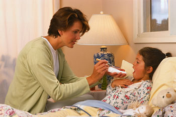 Sick Child Laying in Bed Opens Mouth for Mother Holding a Thermometer 